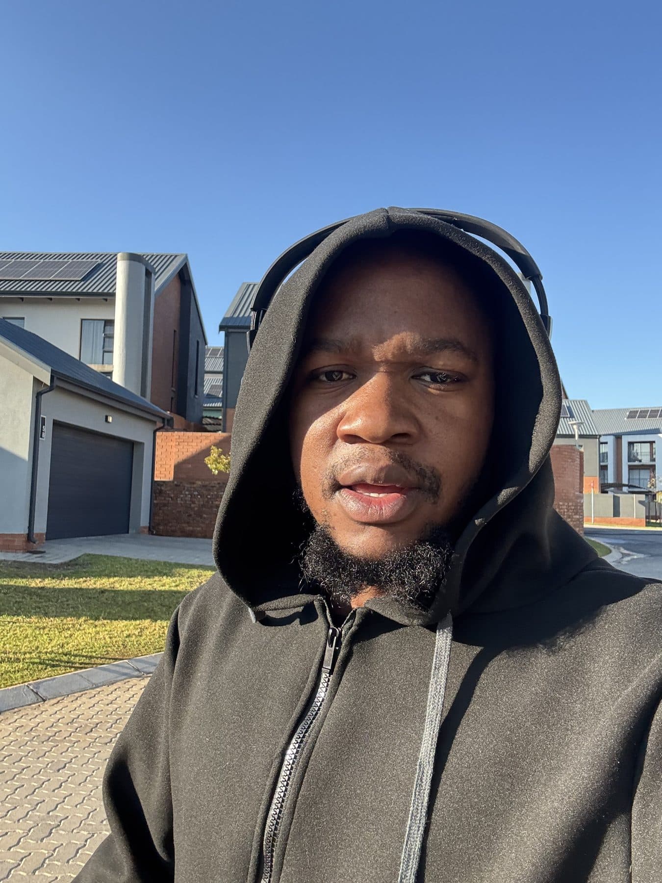 Crecias in a black hoodie and headphones on a sunny street